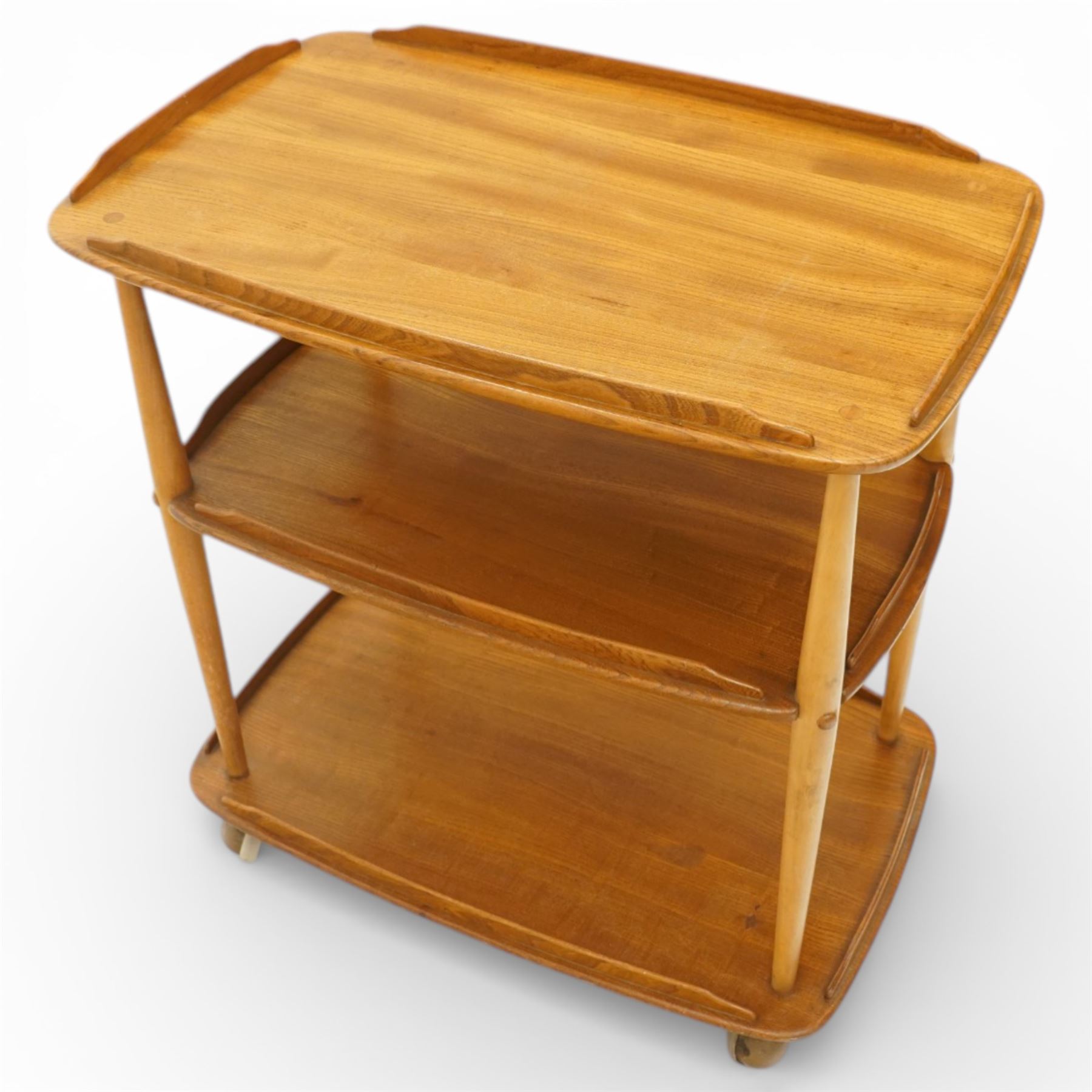 Ercol - elm tea trolley, Model 458. Rectangular three-tier form with shaped gallery edges, supported on turned upright supports, raised on castors