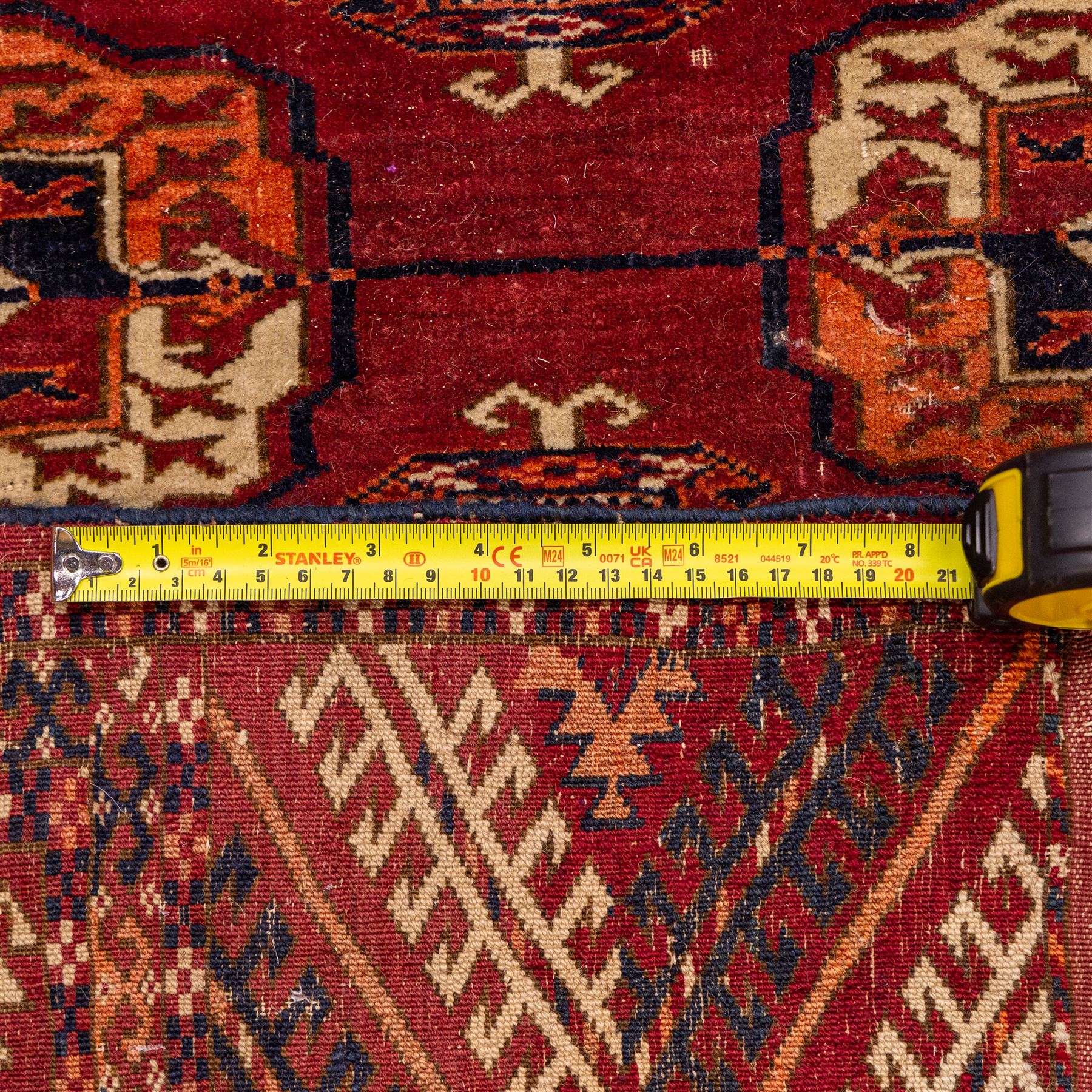 Vintage Bokhara hand-knotted rug, madder field woven in rows of octagonal Tekke guls arranged in vertical columns, each enclosing angular cruciform devices and tribal motifs, divided by narrow indigo lines, within multiple geometric borders incorporating stepped lozenges and latch hook devices, with cotton fringe ends 