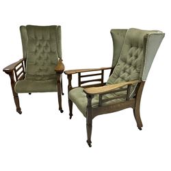 Pair of Arts and Crafts period oak framed wingback armchairs, upholstered in slung buttoned covers, shaped extending armrests on tapering supports terminating to spade feet, on castors  
