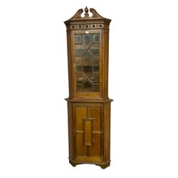 Early 20th century two-sectional oak corner cupboard, swan neck pediment with central architectural column finial, dentil cornice over rosette carving, top section with astragal glazed door enclosing three shelves over single panelled door, on bracket feet