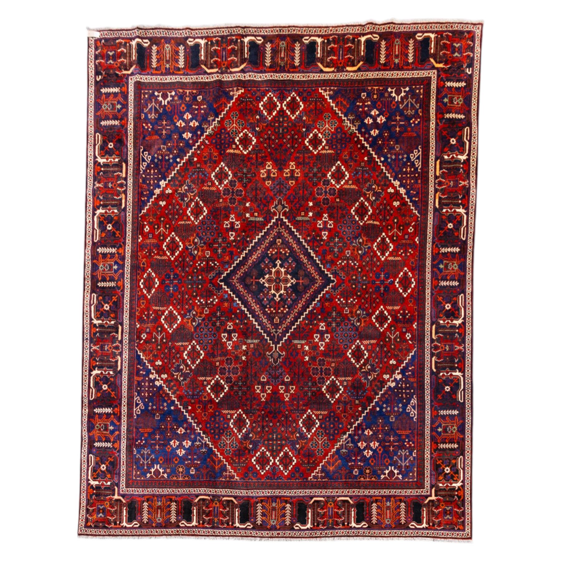Central Persian Joshagen hand-knotted carpet, madder-red field with a central stepped lozenge medallion and densely filled with stylized geometric floral and tree motifs arranged in a repeating lattice enclosed by indigo spandrels and a broad navy border of angular palmette and vine ornament, flanked by multiple guard stripes, cotton fringe ends 