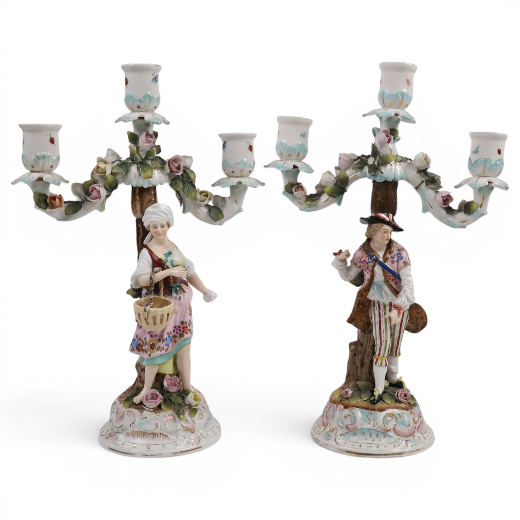 Pair of 19th Century German three-branch figural candlesticks, the figures each in floral dress against a tree, the branches decorated in relief with roses and the sconces painted with insects, H33cm 