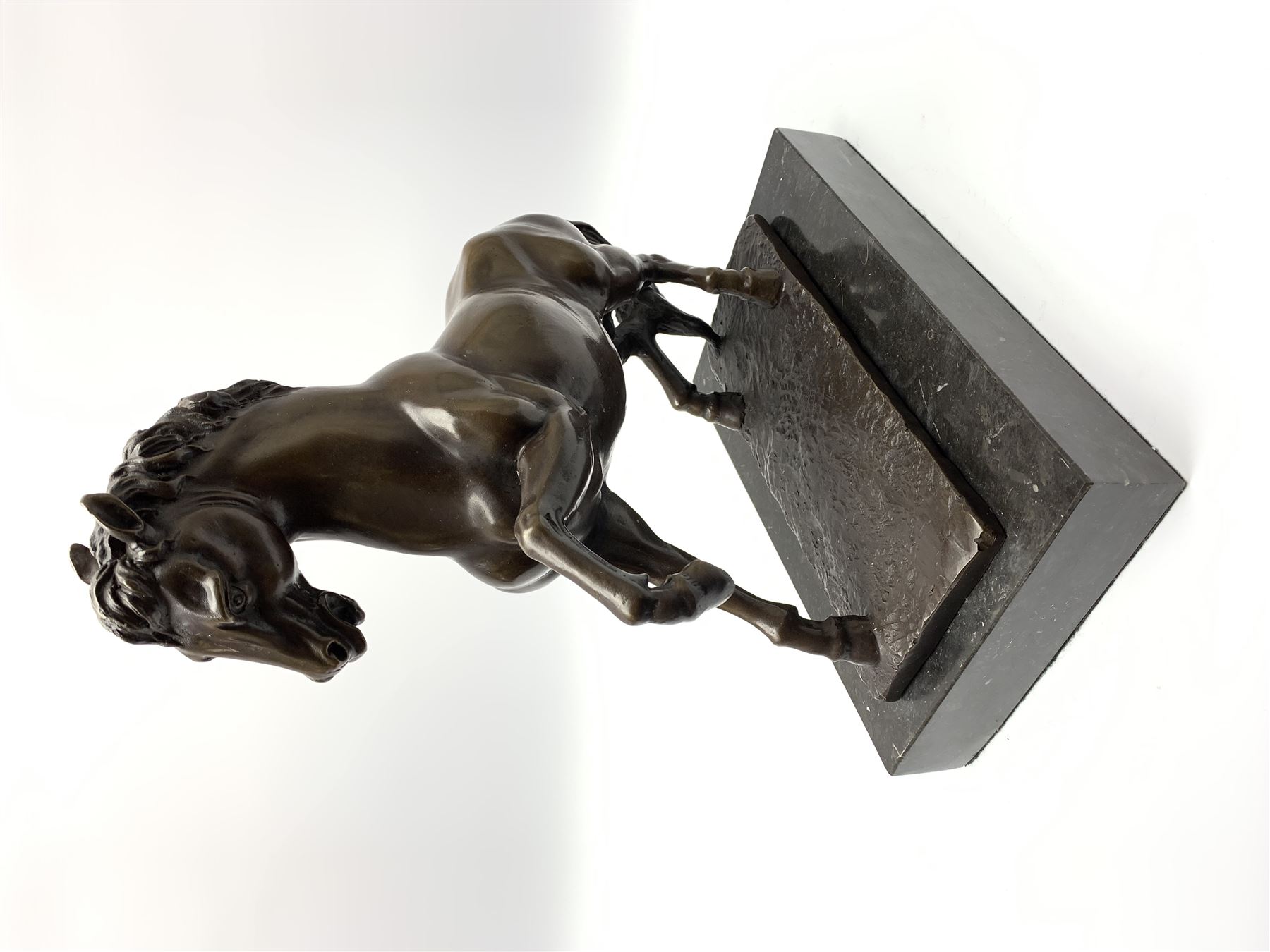 Bronze figure modelled as a prancing horse, upon a naturalistically modelled rectangular base, and black marble plinth, H34.5cm, L31cm