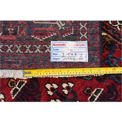 Central Persian Joshaghan hand-knotted carpet, deep red field decorated with a lattice design of stylized boteh and palmette motifs arranged around a stepped diamond medallion, navy corner spandrels similarly decorated enclosed by a dark indigo main border of floral and geometric motifs between multiple guard stripes, with cotton fringe ends 