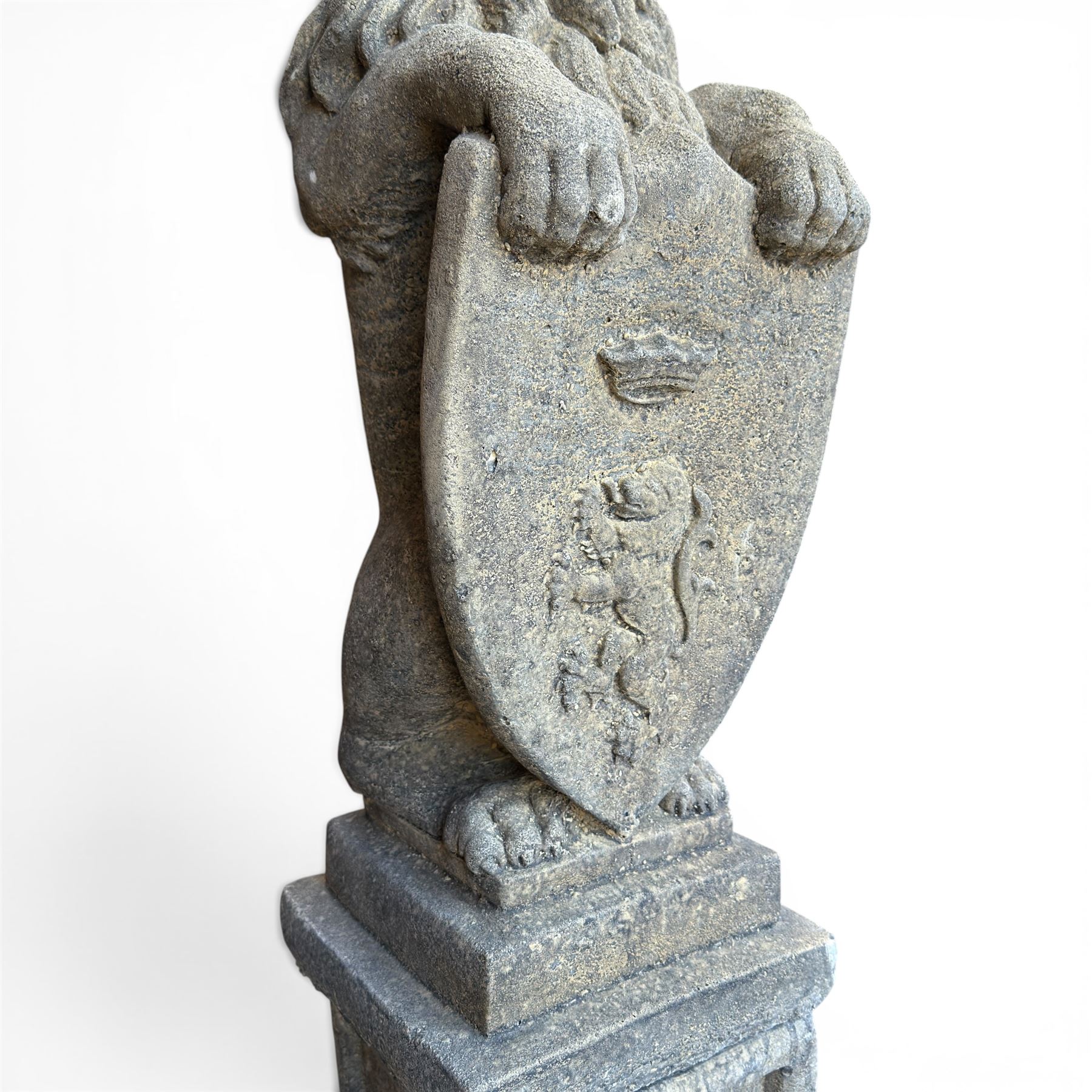 Pair of cast stone Heraldic lions, modelling in upright standing poses with flowing mane, each clasping an Armorial shield moulded with a crowned lion in their forepaws, raised on rectangular pedestals