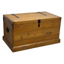 Contemporary polished pine blanket chest, the hinged planked lid with iron strap hinges and clasp fitting, plain boarded sides, fitted with blackened metal drop handles, on a moulded plinth base
