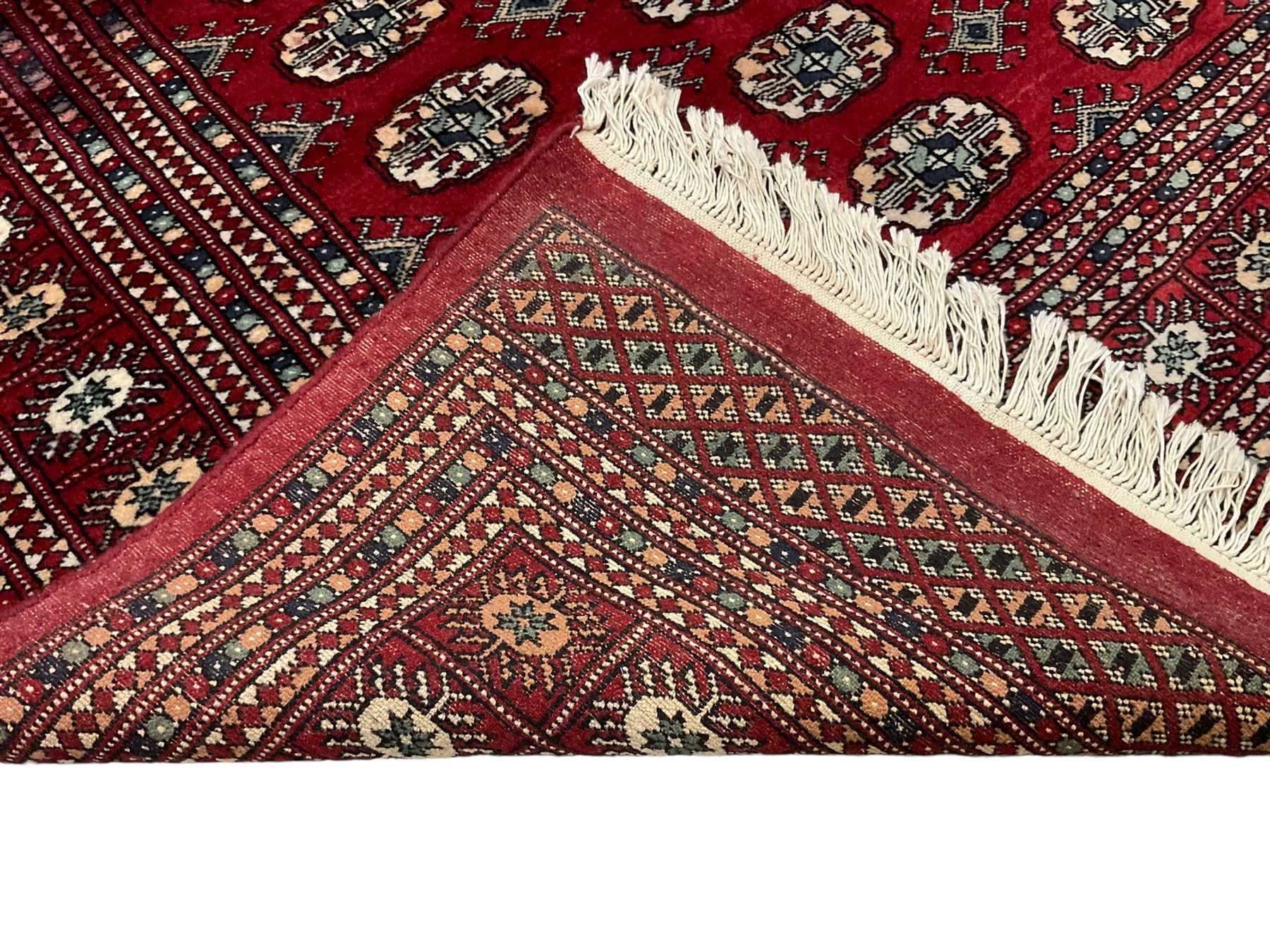 Pakistani Bokhara red ground rug, the field decorated with repeating Gul motifs and lozenges, the multi-band border with stylised plant motifs with dark indigo outlines