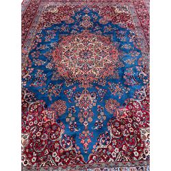 Persian Kirman blue and crimson ground carpet, the field decorated with floral design rosette medallion, the spandrels with scrolling leaf and stylised plant motifs, guarded border decorated with scrolling foliate and flower head motifs, signature panel to one end