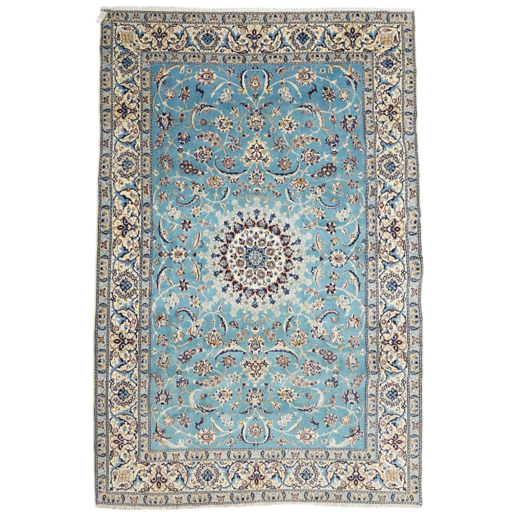 Central Persian Nain hand-knotted carpet, soft sky blue ground with central cusped medallion of radiating palmette form, issuing scrolling vine work, arabesques, and delicate floral sprays, spandrels of conforming design, main border of ivory ground decorated with scrolling vine work palmettes and stylized floral motifs, flanked by narrow guard stripes, with cotton fringe ends 