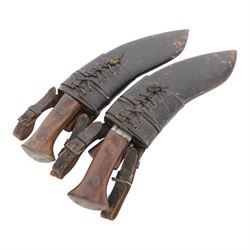 Two WWII Kukri knives, wooden grip with brass cap to pommel, single edged curved blade, within leather scabbard with belt attachments, overall L40cm 