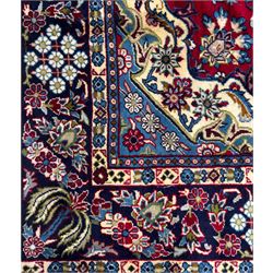 Central Persian Isfahan Carpet, hand-knotted, featuring a bold central rosette medallion on a rich red field, flanked by stylised floral sprays, scrolling foliage and mythical animals, within a broad indigo border decorated with alternating cartouches and flowerheads