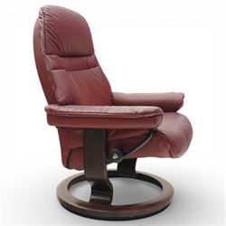 Ekornes - Stressless reclining armchair and matching footstool, upholstered in oxblood leather with padded headrest and segmented back cushion, shaped armrests with exposed adjustment handles, raised on stained laminated beech circular swivel base, the conforming stool on matching ring base