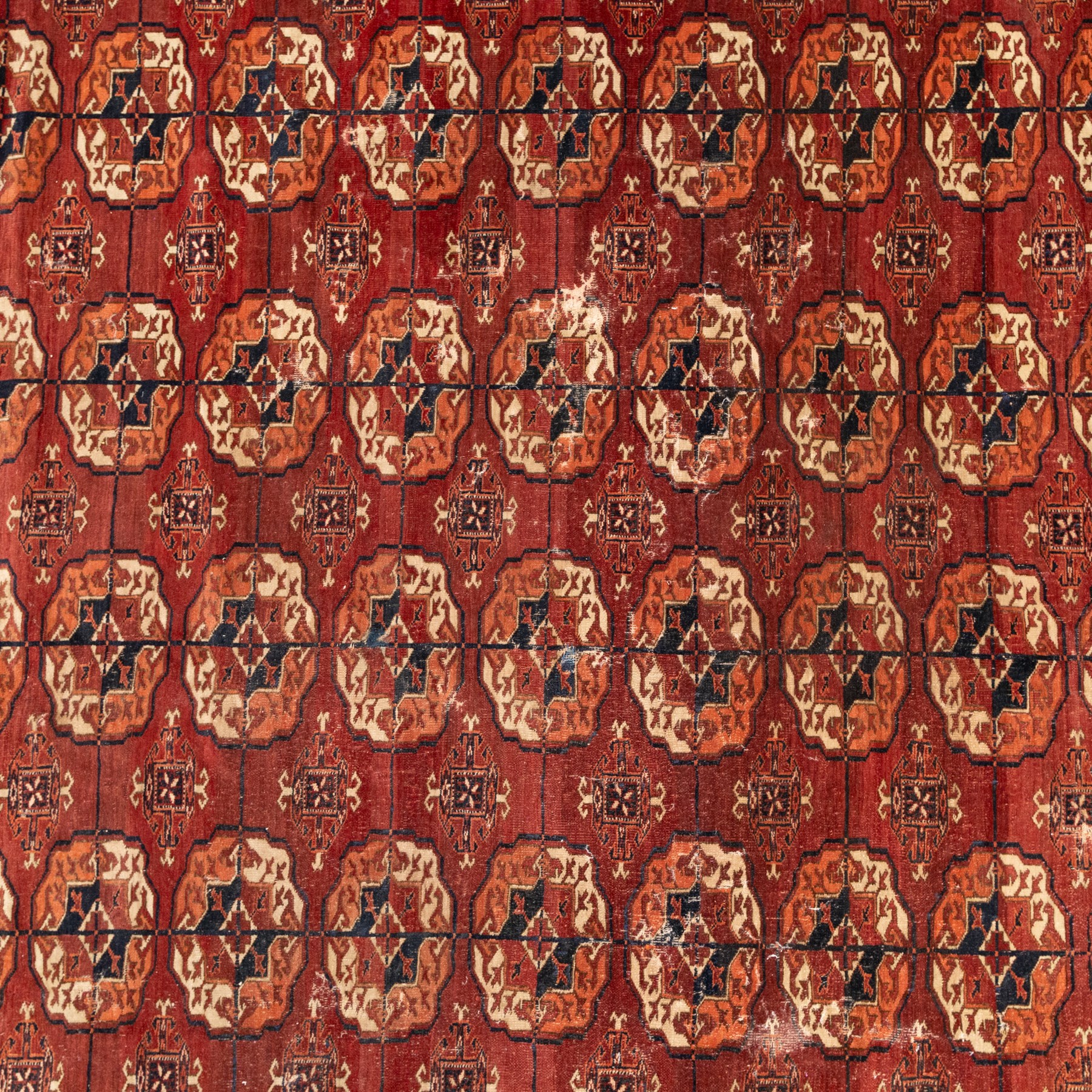 Persian Bokhara crimson ground rug, the field decorated with five rows of repeating Gul motifs with interspersed geometric design, enclosed by a guard band of further geometric-style Gul designs comprised of hook motifs