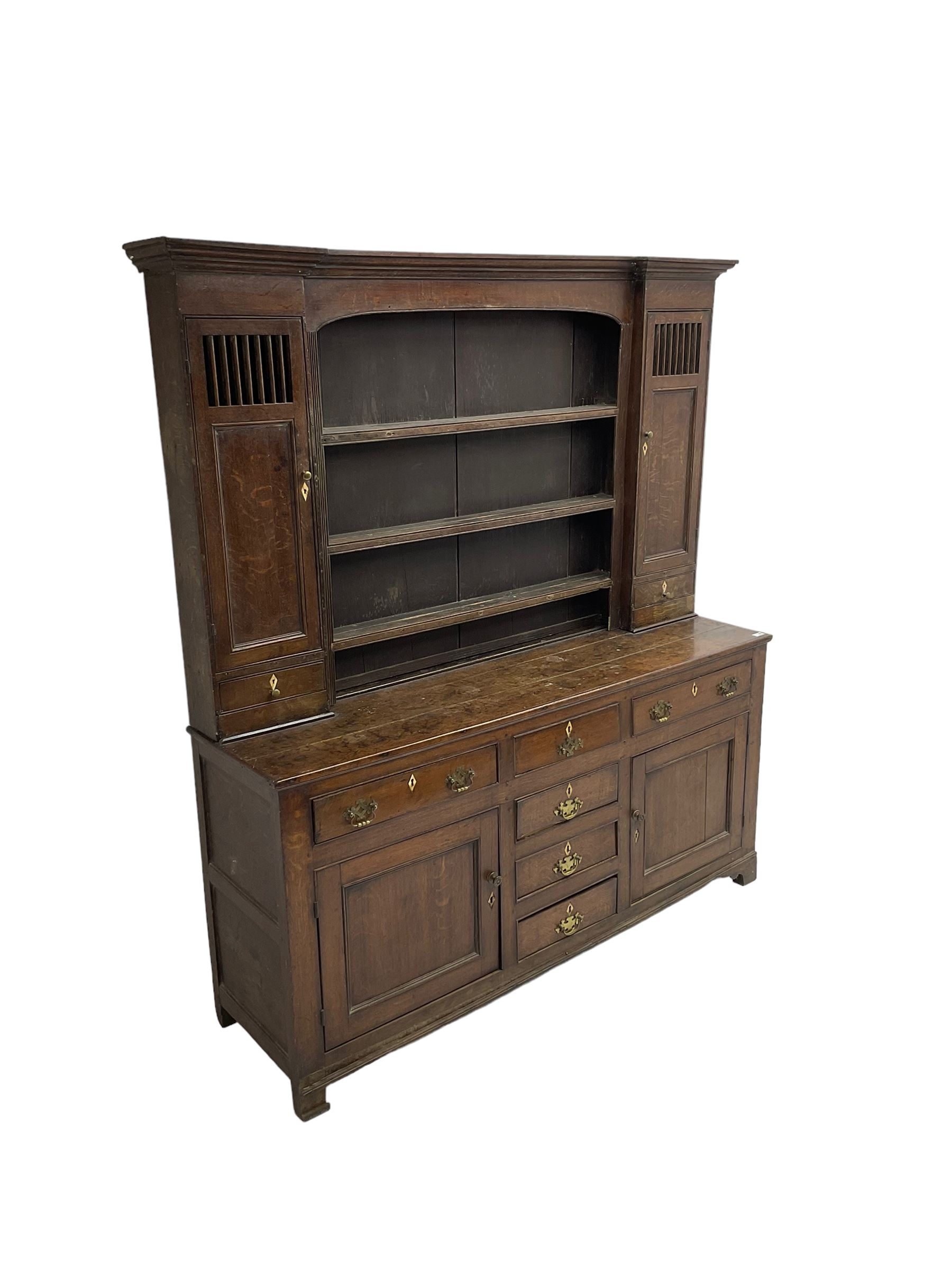 George III oak dresser, projecting cornice over three tier plate rack flanked by reeded uprights and two cupboards, enclosed by slatted and panelled doors above small drawers, the lower section fitted with six drawers and two cupboards, on bracket feet