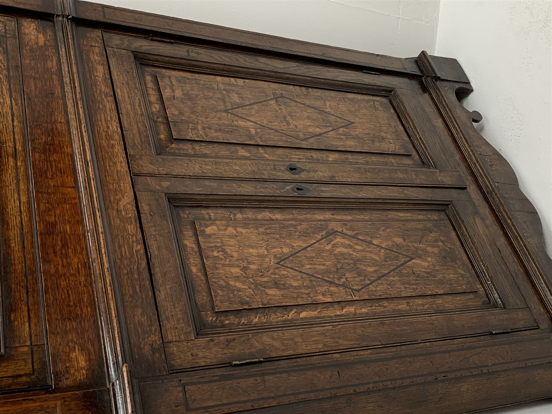 George III oak floor standing corner cabinet, scrolled swan neck pediment with central finial over astragal glazed door, painted interior fitted with three shaped shelves, the lower section fitted with single shaped shelf enclosed by two fielded panel doors inlaid lozenges, on bracket feet, H195cm, W77cm