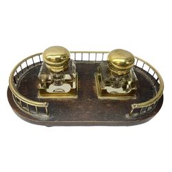 Early 20th century oak desk stand, of oval form with brass gallery and twin brass square sections, holding two removable clear glass inkwells with brass hinged covers, the whole upon four brass compressed bun feet, L30cm