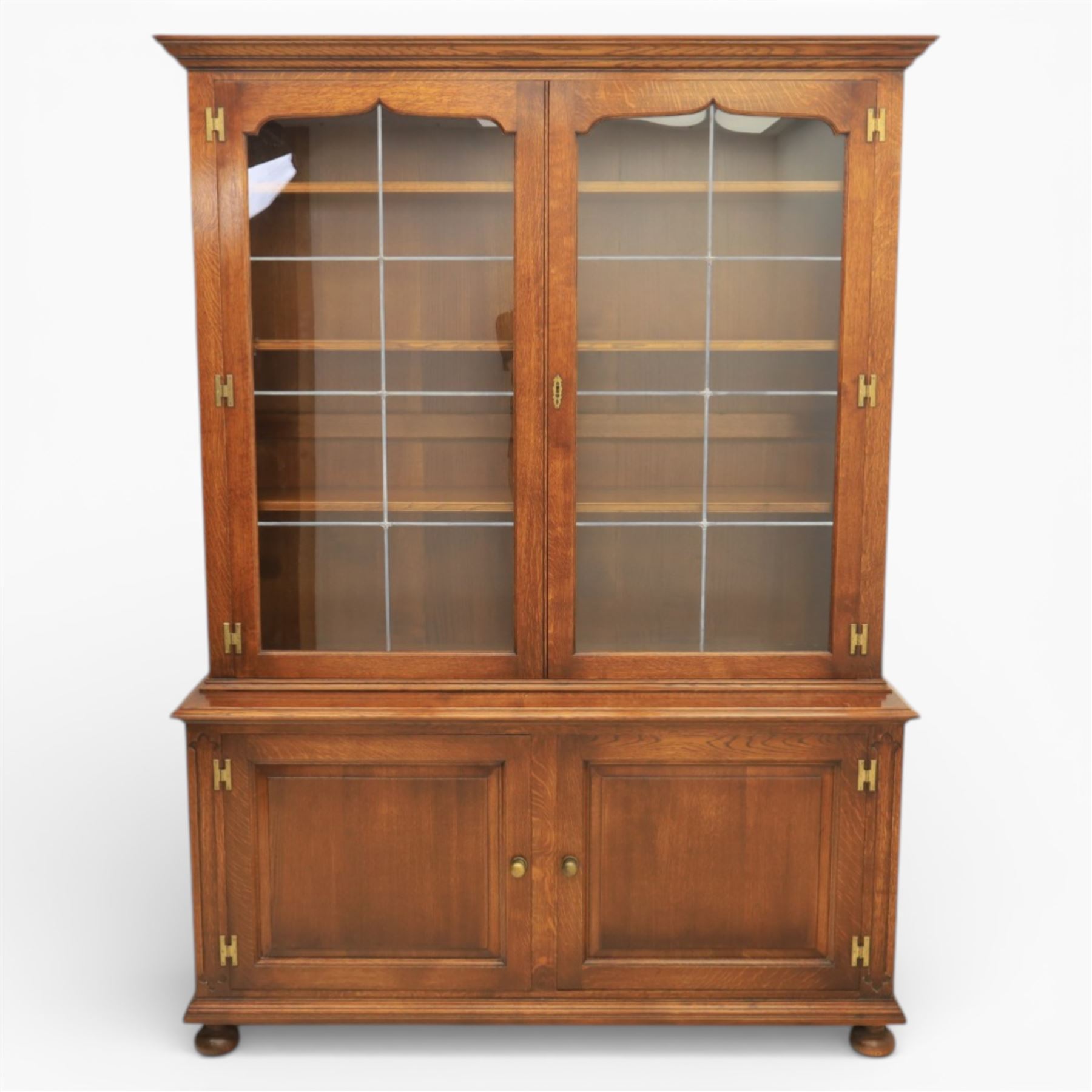 Late 20th century oak bookcase on cupboard, with moulded cornice above pair of astragal glazed doors with shaped inner frames enclosing adjustable shelves, the base with moulded top above two fielded panel cupboard doors with brass handles, upon compressed bun front feet 