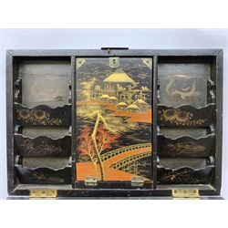  A 20th century Chinese black lacquer and gilt detailed writing box, decorated with figures, pagodas and cranes amidst a mountainous landscape, the hinged cover opening to reveal a compartmented interior and fold out baize lined slope, H20cm L46.5cm D31.5cm.   