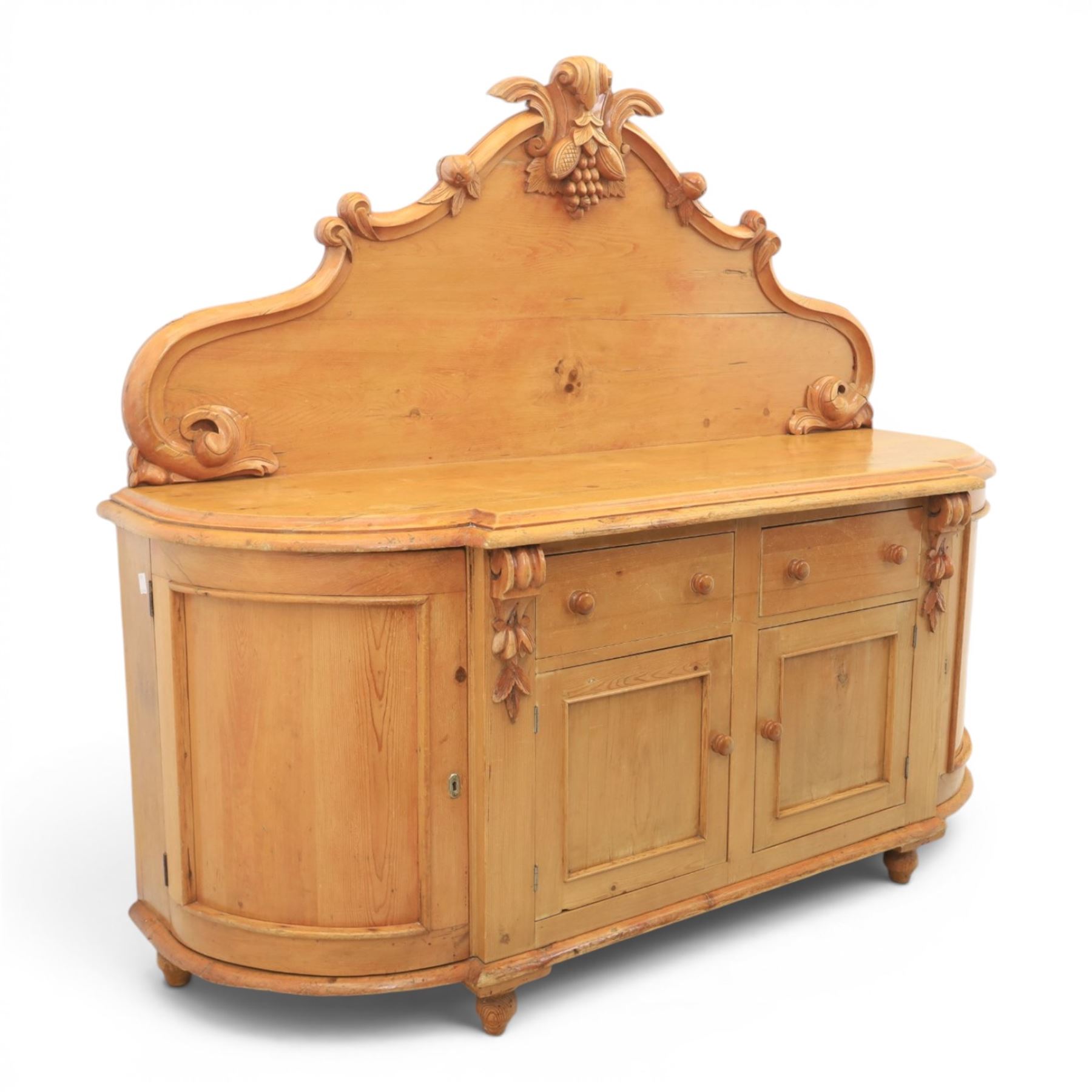 Victorian pine chiffonier, shaped moulded top with raised scroll carved back surmounted by carved fruit and foliate crest, fitted with two frieze drawers over two panelled cupboard doors, the outer cupboards of bowed form, carved foliate corbels, on plinth base