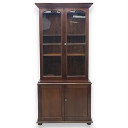 20th century mahogany display bookcase, projecting moulded cornice over a pair of glazed doors with shaped upper glazing and plain lower panes, opening to reveal shelved interior, the base with two recessed panel cupboard doors, raised on a moulded plinth with compressed bun feet