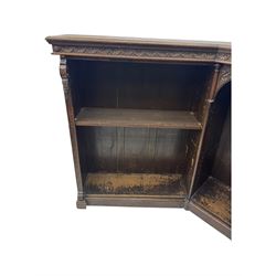 Victorian carved oak corner bookcase, L-shaped form, moulded top over lunette carved frieze, decorated with S-scroll and mask carved corbels with trailing acanthus leaves, fitted with adjustable shelves, on moulded plinth base 