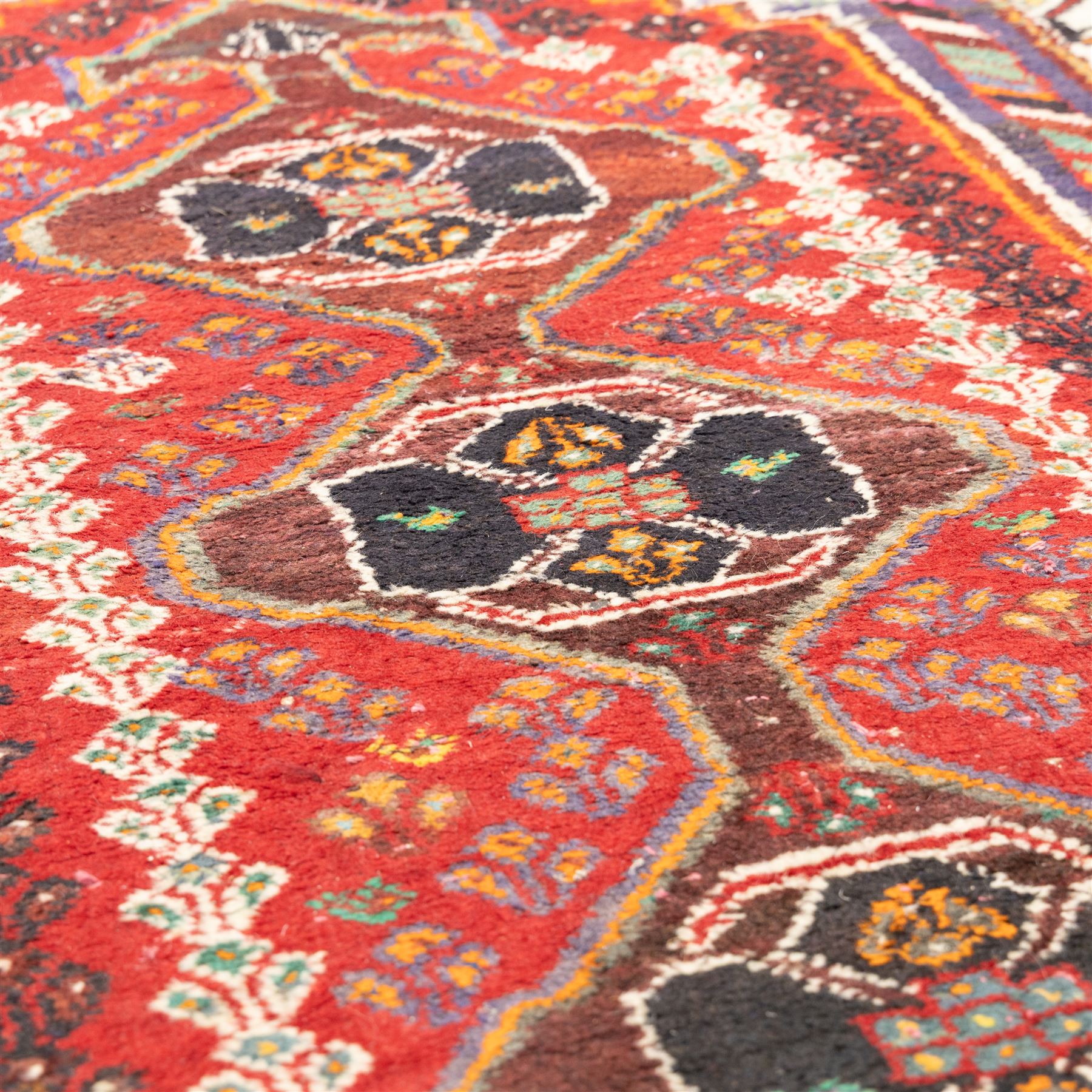 Northwestern Persian village rug, madder red field, with serrated central panel enclosing three linked lozenge medallions, polychromed spandrels, ivory border, and geometric guard stripes  