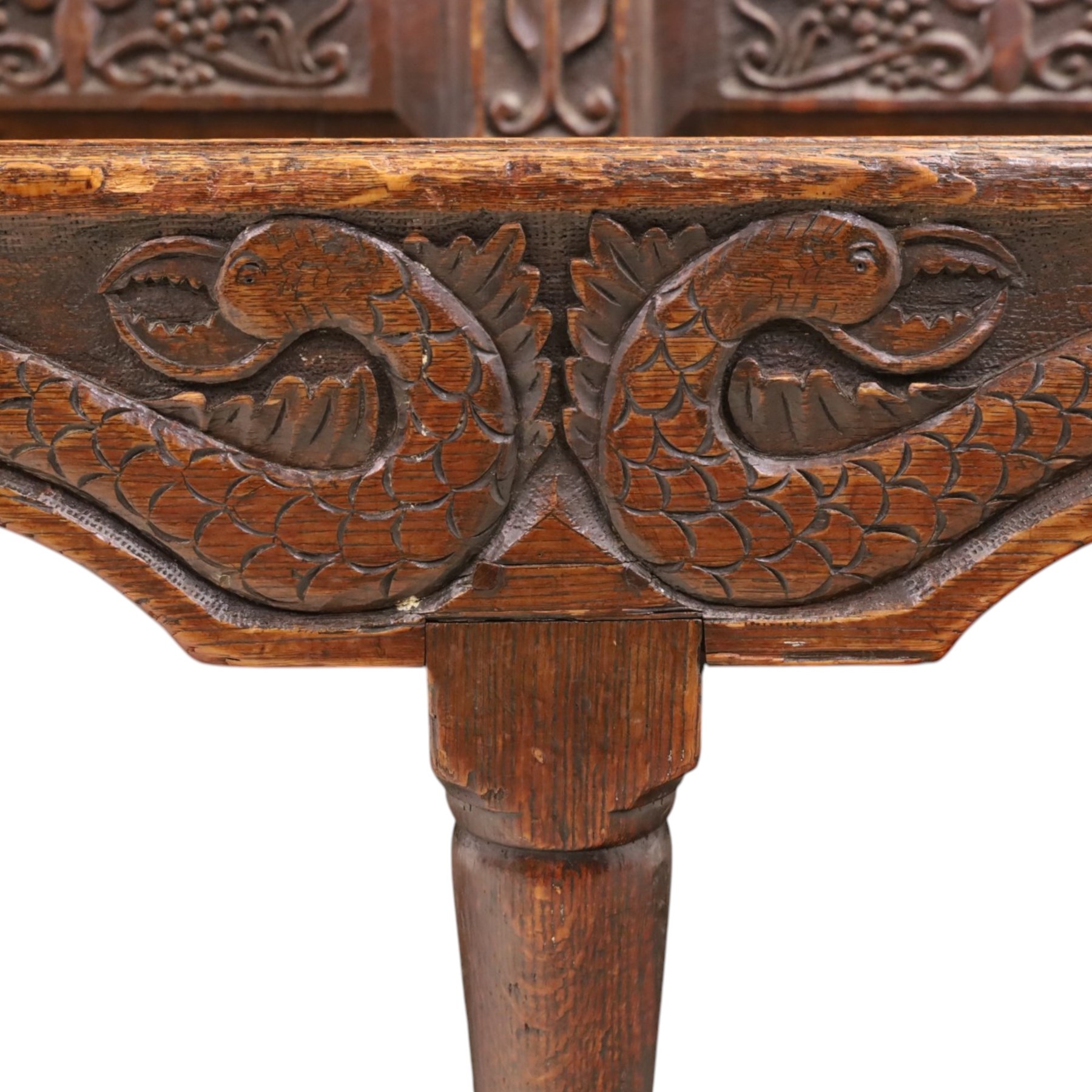 19th century Gothic Revival heavily carved oak settle or hall bench, the high quadruple back with moulded cresting rail over a frieze carved with stylised dolphin and sea creature motifs, the panels decorated with griffin and bird motifs with floral dividing rails, the shaped apron similarly carved with scaly sea beasts, on three cabriole front-supports united by stretchers