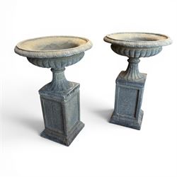 Pair of cast stone garden urns of kylix form on pedestals, the broad egg-and-dart moulded rim over a shallow gadrooned underbelly, with waisted tapering base, raised on matching plinth bases with faux panelled facia