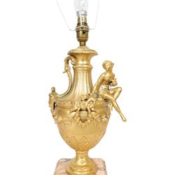 Pair of Rococo style gilt metal table lamps, the urn shaped bodies each with applied figure seated upon shoulder, and female mask to opposite side issuing scroll leading to top of neck, the body cast and applied with stiff leaf detail, and foliate swags and wreaths, upon square pink marble plinths with applied gilt metal mask mounts, and four gilt metal bracket feet, each supported a pleated cream silk closed top lampshade, H63cm
