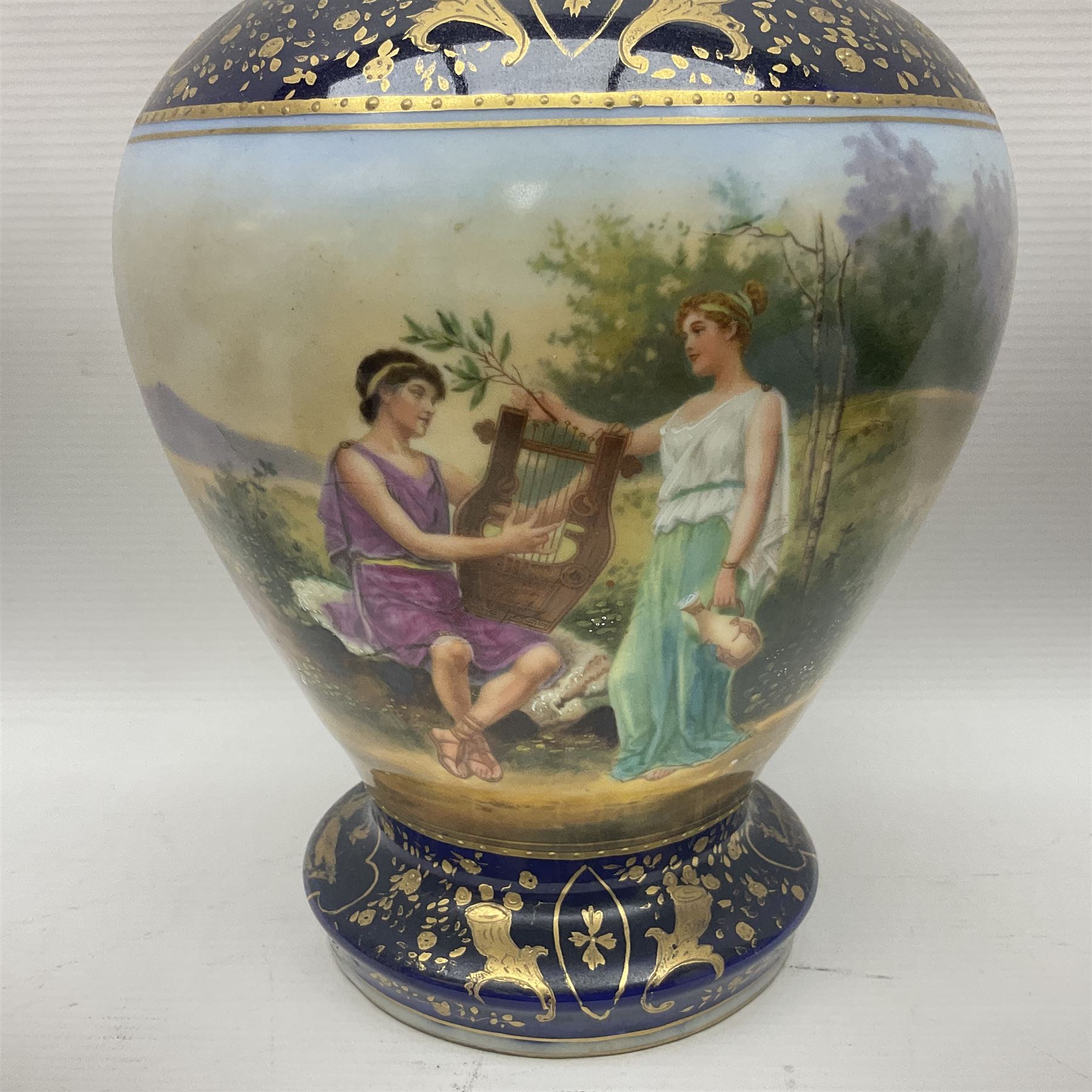 19th century Vienna style porcelain 'Musik' garniture, the central vase of baluster form with domed cover flanked by two smaller vases with twin curved gilt handles to short neck, each decorated with classical figural vignettes between blue borders heightened with gilt, H33.5cm