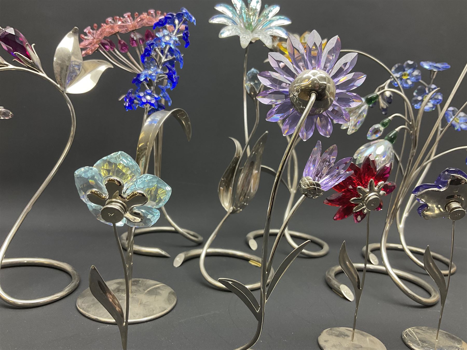 Eleven Swarovski Crystal flowers, to include violet, sunflower, delphinium, forget-me-not and lily-of-the-valley, each on stylised metal stems, tallest H23cm