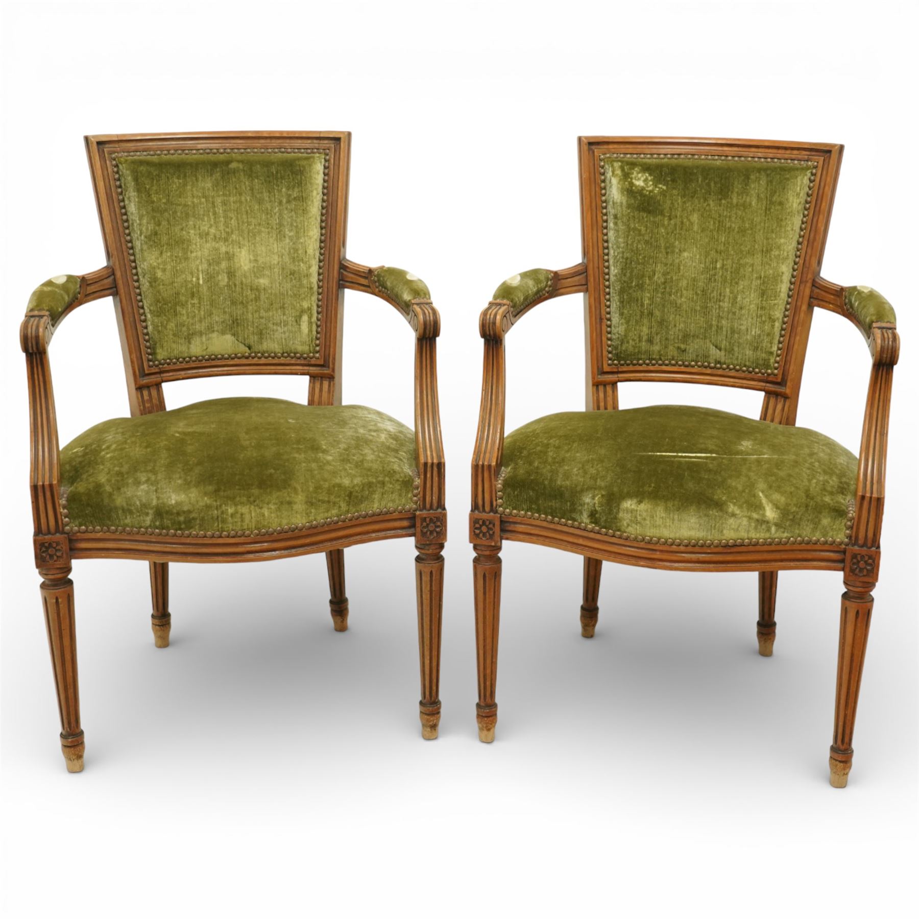 French Louis XVI style walnut armchairs, rectangular upholstered backs with nailhead trim, padded seats upholstered en suite, out-swept arms with upholstered pads, fluted supports with carved rosettes to the knees, on turned and fluted tapering legs