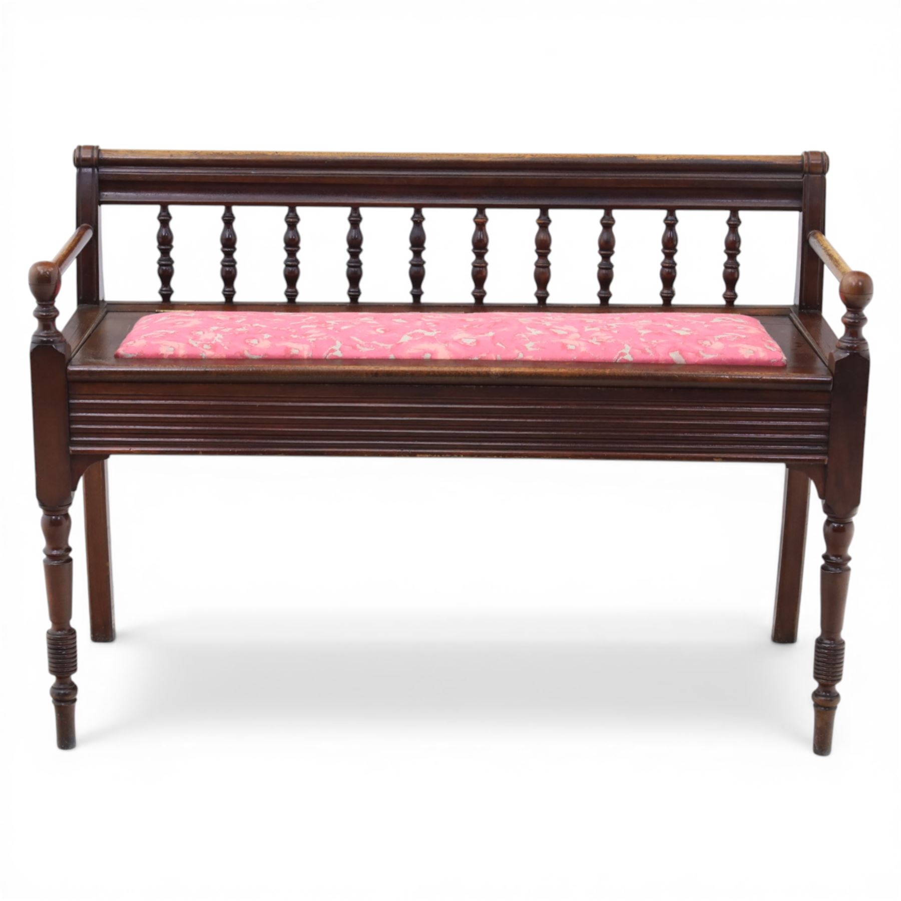 Early 20th century mahogany hall bench, spindle turned back with shaped top rail and open arms terminating in ball finials, upholstered seat within a fluted frieze, raised on turned tapering supports