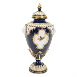 Late 19th century Royal Worcester porcelain vase and cover, circa 1897, of baluster form with twin lion masks to shoulders, painted with a reserve of exotic birds within a landscape, against a blue scale ground with gilt highlights, and further detailed with smaller reserves containing butterflies, the shoulder, base of body and foot with moulded acanthus bands, upon a circular spreading foot, with green printed marks beneath including shape number 2305 and Rd no 419210, H27.5cm