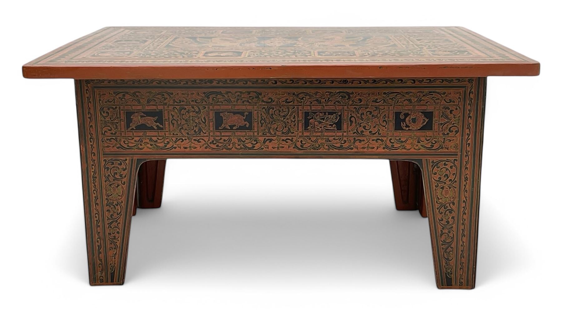 Late 20th century Burmese low table, the rectangular top and frieze decorated in traditional Shwezawa lacquer with gilded celestial figures, mythological beasts and dense foliate scrollwork, the folding base with hinged slab supports bearing conforming decoration