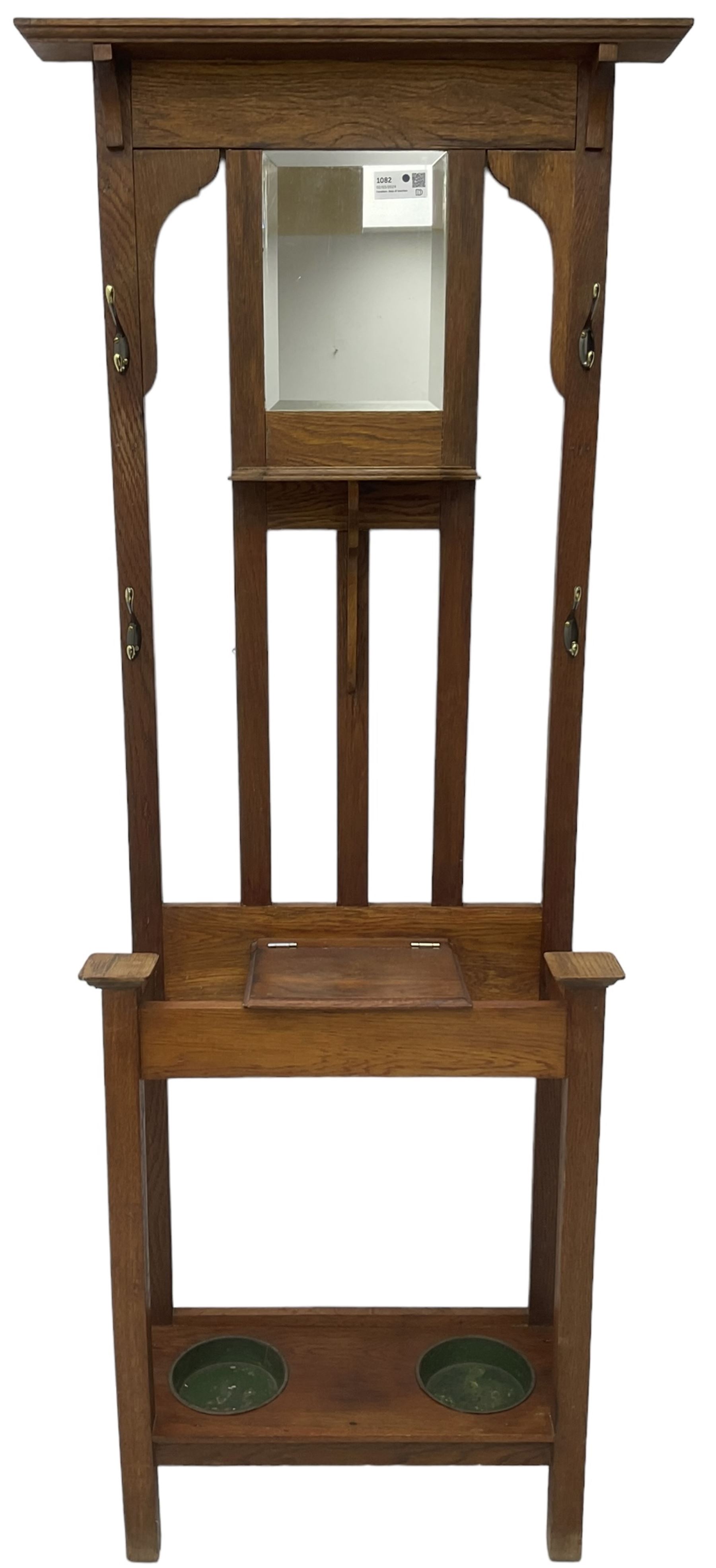 Edwardian oak hall stand, raised back with rectangular bevelled mirror plate surrounded by shelf and coat hooks, fitted with a glove box with hinged lid, over an undertier with two inset umbrella drip trays