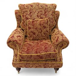 Duresta – pair of armchairs, upholstered in red and gold damask fabric with piped edges, scroll arms and loose feather-filled cushions, raised on turned wooden feet with brass castors