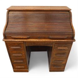 Early 20th-century oak roll-top desk with tambour shutter, enclosing a fitted interior of pigeon holes and small drawers, and pedestal base fitted with nine drawers with moulded handles, raised on plinth base 
