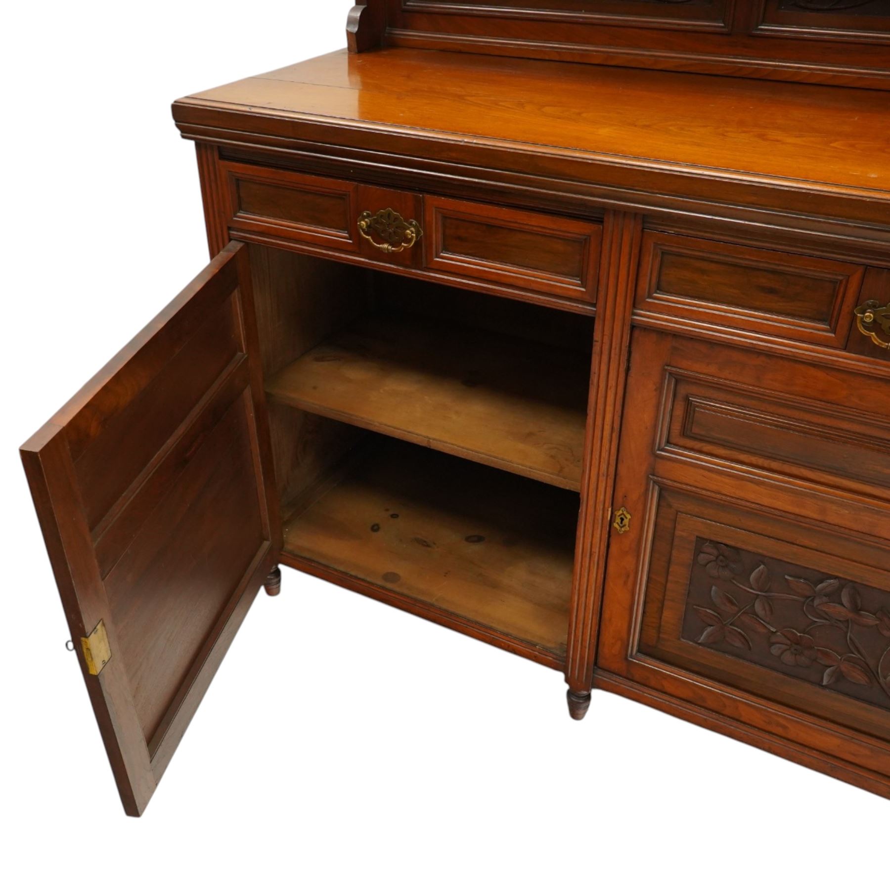 Late Victorian mahogany mirrored back sideboard, the mirror back with three bevelled mirror plates above a single shelf, rectangular moulded top over two frieze drawers with brass handles, above a twin panelled cupboard, carved recessed panels decorated with flowers and foliage, fluted uprights, raised on turned feet