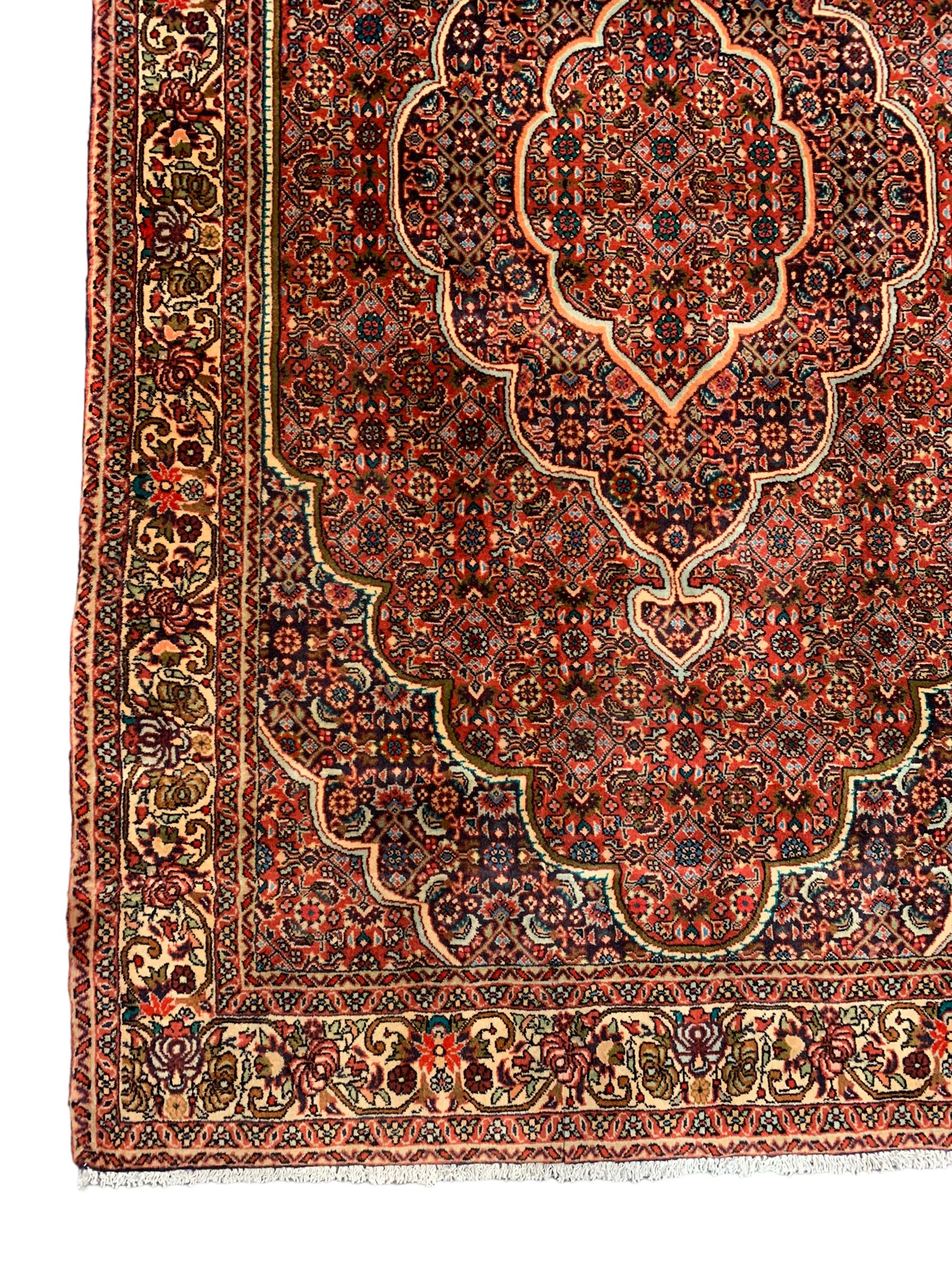 Persian Bidjar crimson ground rug, thick woollen pile, the field decorated with repeating Herati motifs within cusped outlines, the guarded border decorated with repeating flower head motifs