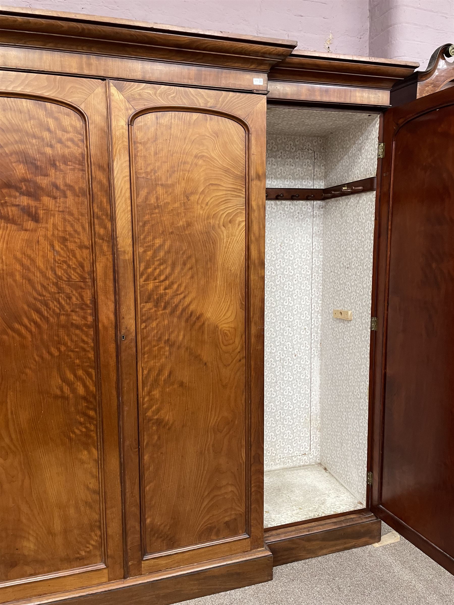19th century figured mahogany quadruple breakfront press wardrobe, projecting cornice with banded frieze over arch panelled doors, the interior fitted with three sliding trays over two short and three long graduating drawers with recessed brass handles, flanked by two hanging cupboards with hooks