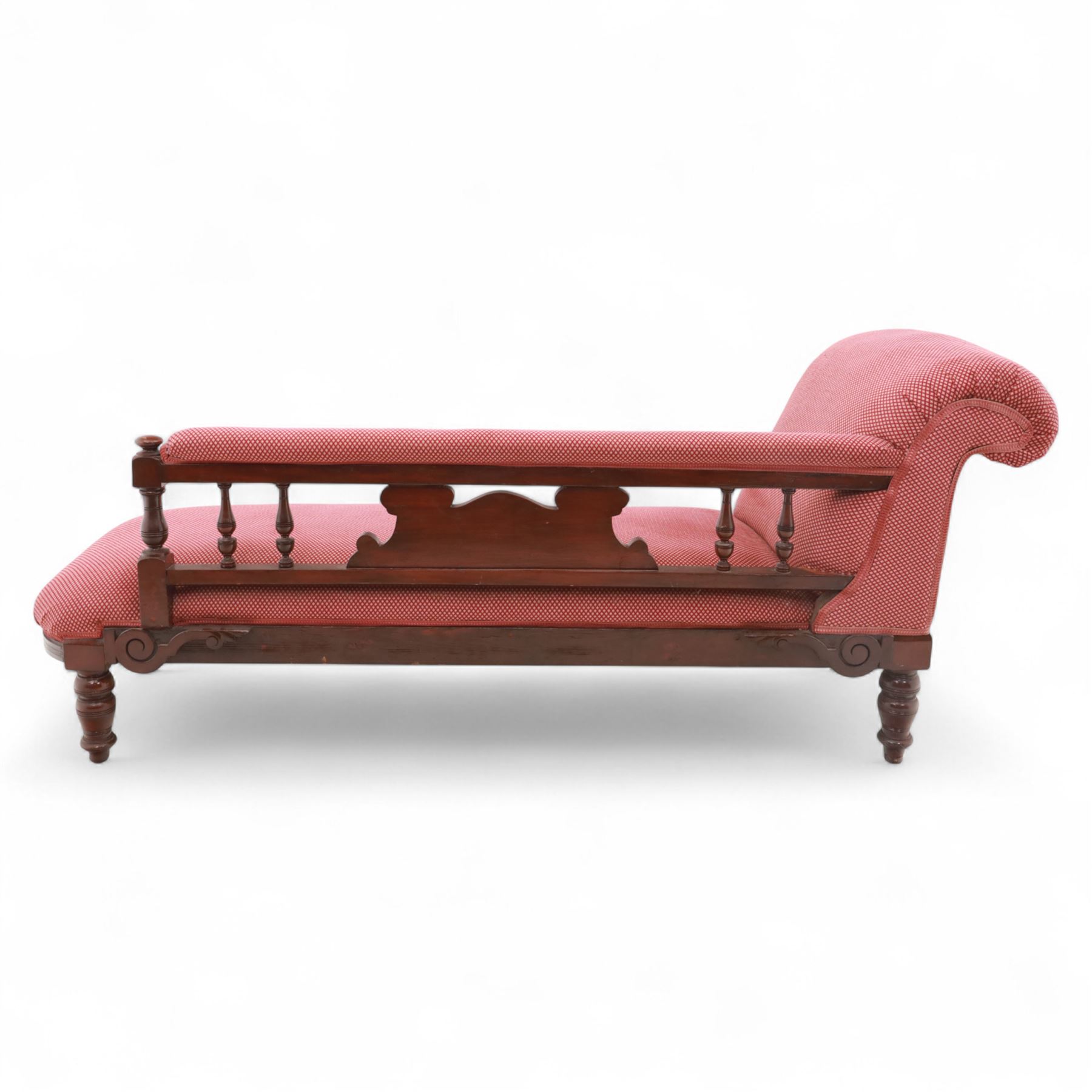 Late Victorian mahogany chaise longue, of scroll-ended form, upholstered in red diamond-patterned fabric with padded back and scroll-carved support, open arm with carved foliate and turned upright, raised on turned tapering legs 