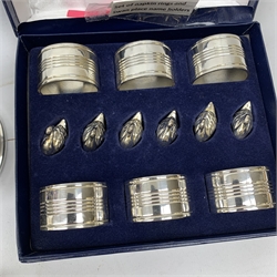  A cased silver plated set of six napkin rings and menu holders modelled as swans, together with a cased silver plated cruet set comprising pepper, open salt and mustard with blue glass liners, and spoons, a small Elkington silver plated toast rack, and a silver plated preserve jar with stylised figural pierced decoration and blue glass liner.   