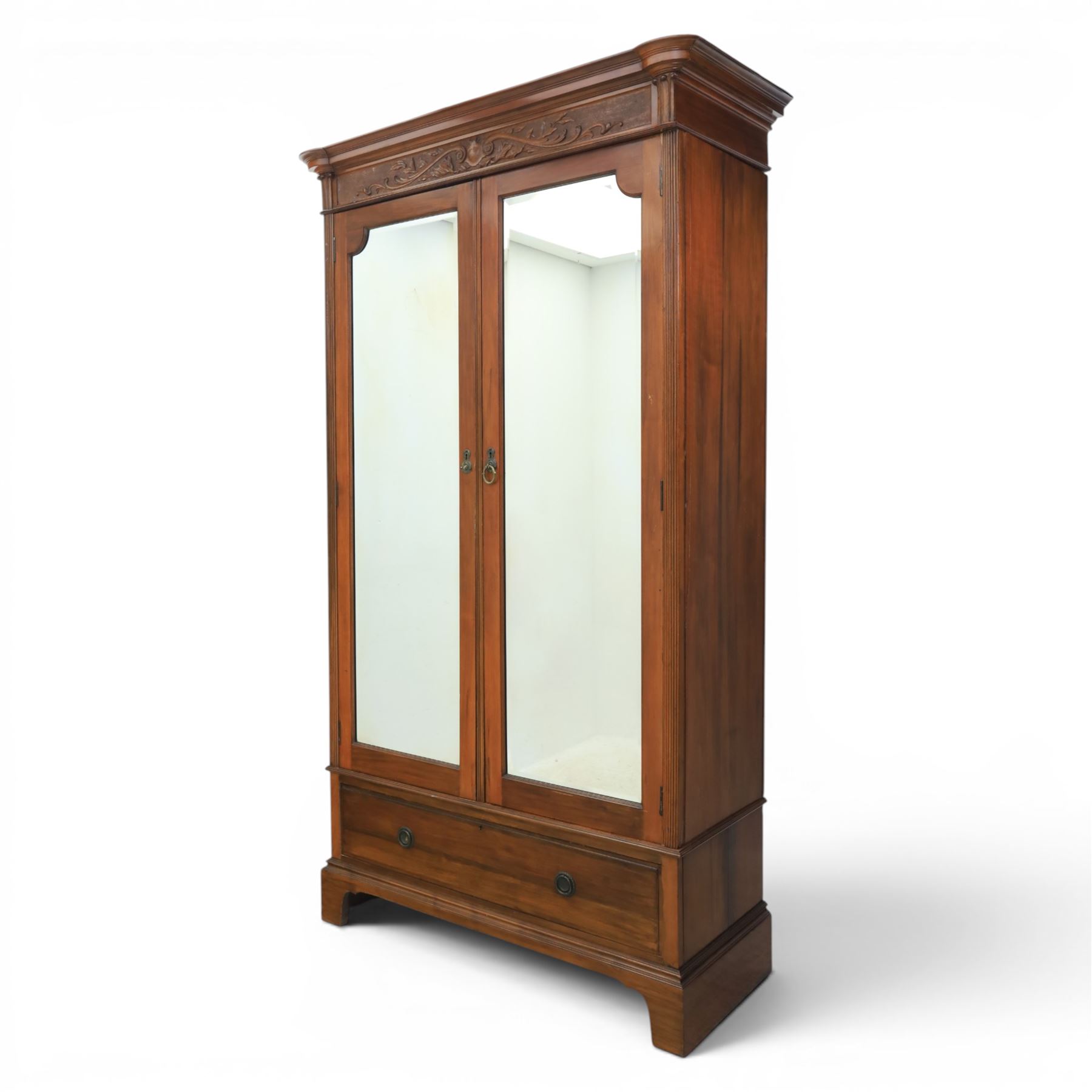 Edwardian walnut double wardrobe, featuring two mirrored doors with bevelled plates, carved frieze with fluted pilasters, above single base drawer
