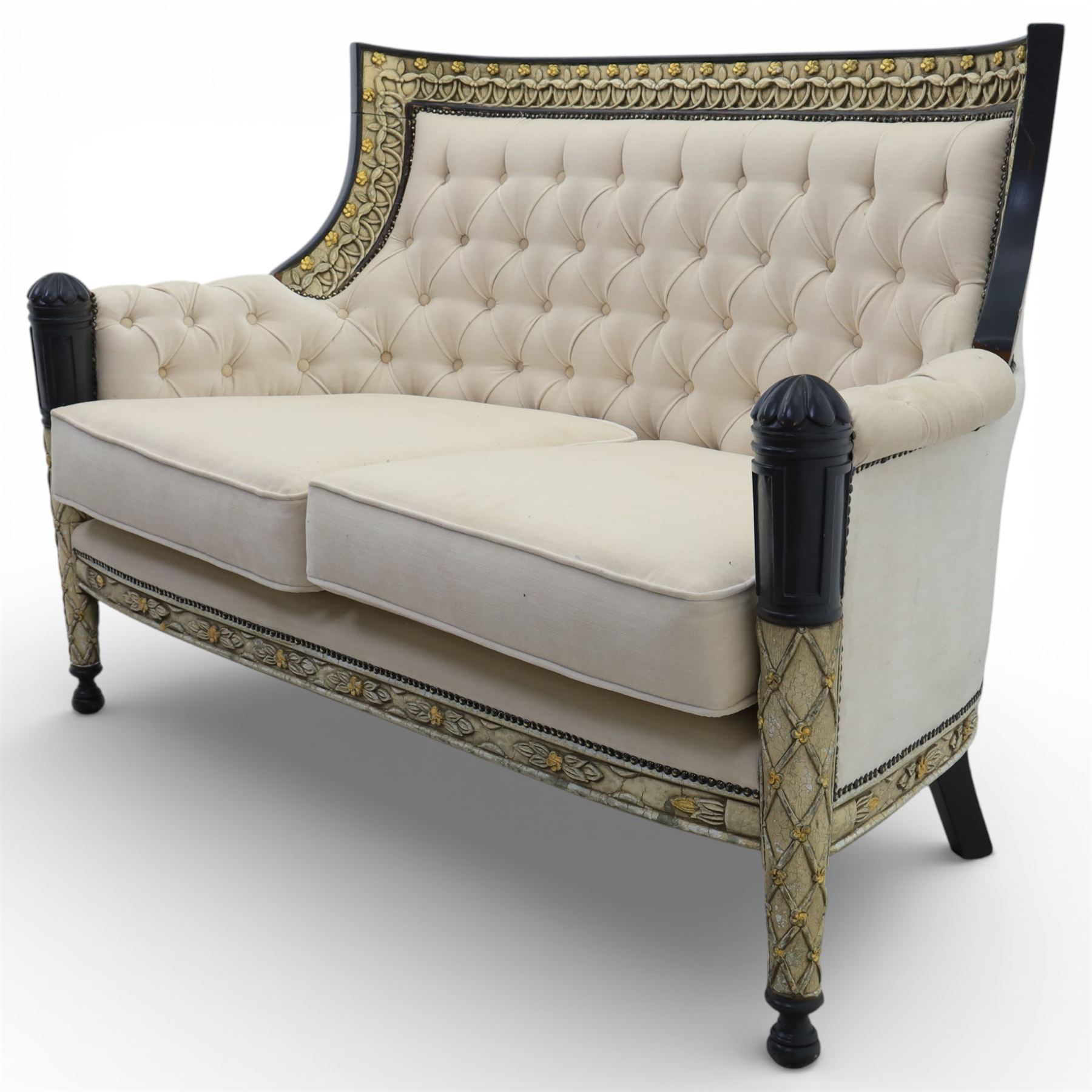 20th century Louis XVI style settee, upholstered in cream fabric with buttoned back and arms, and plain seat cushions, the shaped and black painted frame with entwined foliate detail and gilt flower heads, upon column legs with bun feet