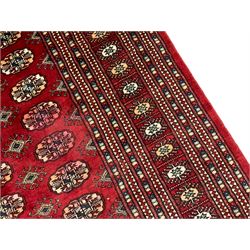 Pakistani Bokhara red ground rug, the field decorated with repeating Gul motifs and lozenges, the multi-band border with stylised plant motifs with dark indigo outlines
