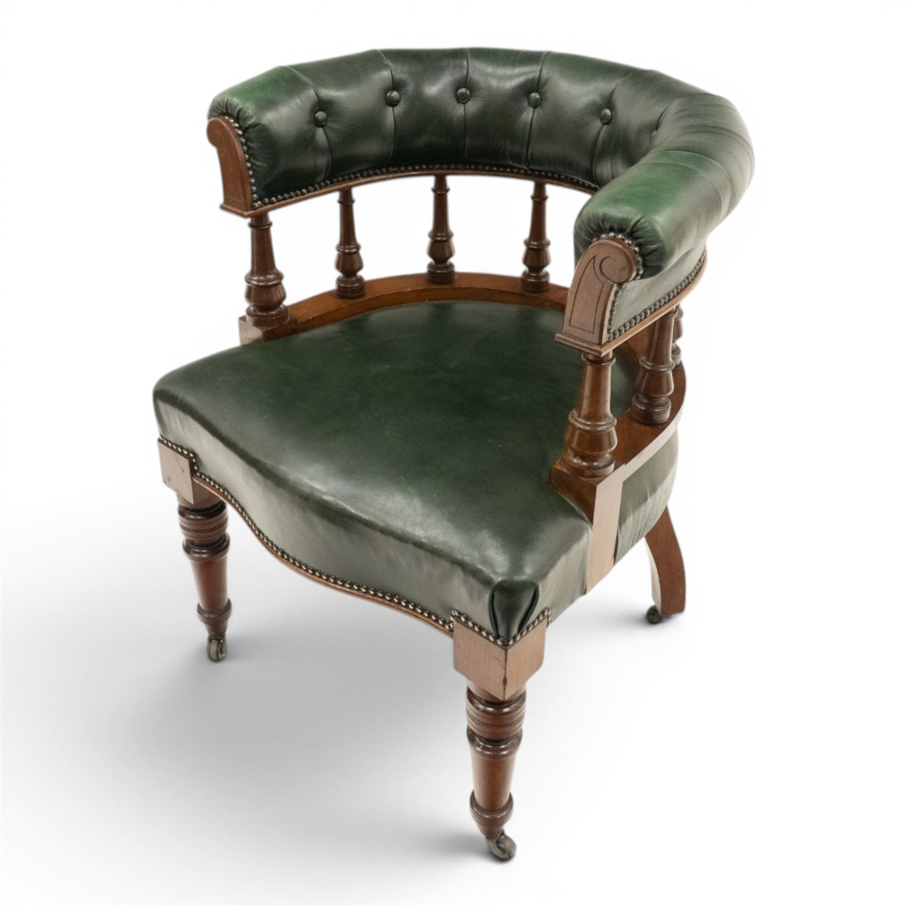 Late Victorian mahogany framed Captains tub desk chair, the green leather upholstered cresting rail over turned spindle supports over a sprung seat, raised on front turned supports terminating to ceramic castors