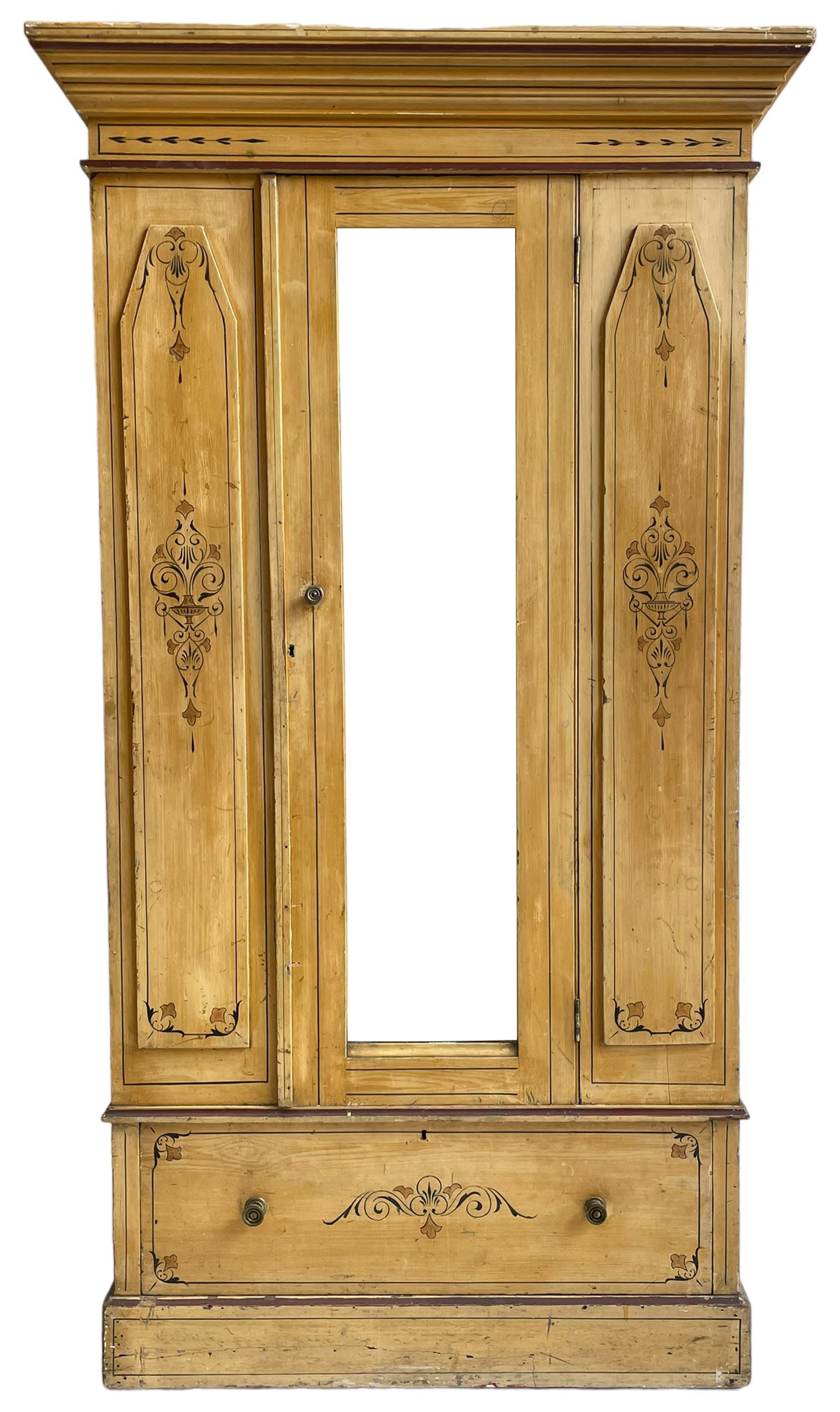 19th century painted pine wardrobe, the projecting cornice over mirror glazed door, with painted decoration depicting scrolling foliate and urns, drawer to base on skirt