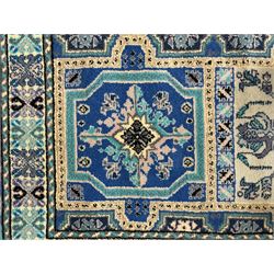 Morrocan single weft blue ground rug, the field segmented into a grid of ten rectangular panels, bordered by a series of guard bands with repeating floral and geometric patterns with interlocking vines and rosettes, the edges finished with a fringe of twisted tassles