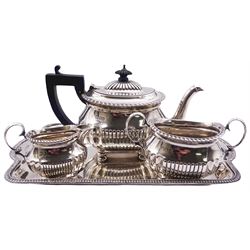 Late Victorian three piece bachelors tea service, comprising teapot with ebonised handle and finial, twin handled sucrier, and milk jug, each of oval part fluted form with oblique gadrooned rim, upon four ball feet, hallmarked Charles Start Harris, London 1899, together with a late Victorian tray with oblique gadrooned rim, hallmarked Mappin & Webb, Sheffield 1892, approximate gross weight 37.10 ozt (1154 grams)
